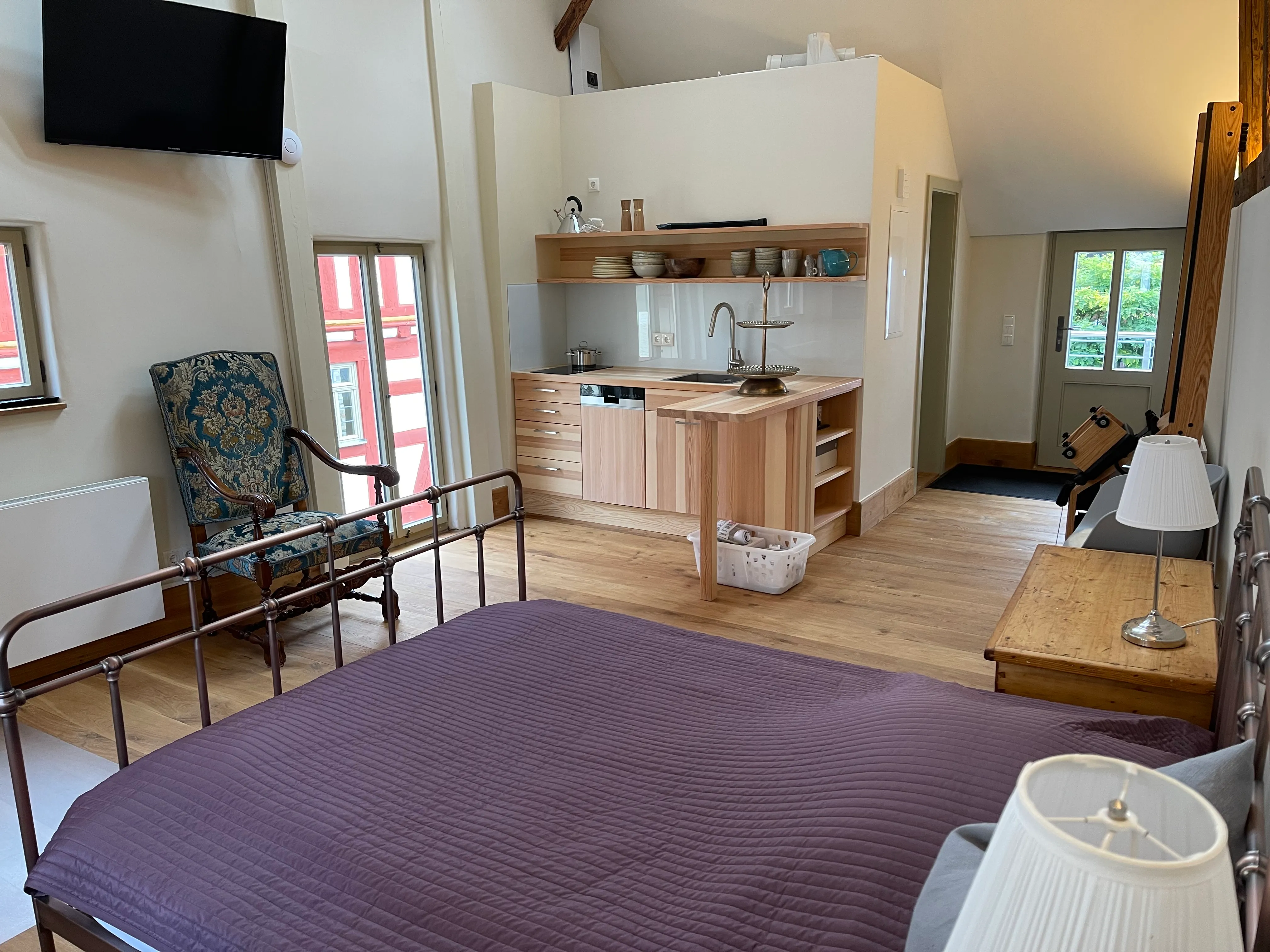 Offener Wohnraum mit Bett, Küchenzeile und antikem Sessel