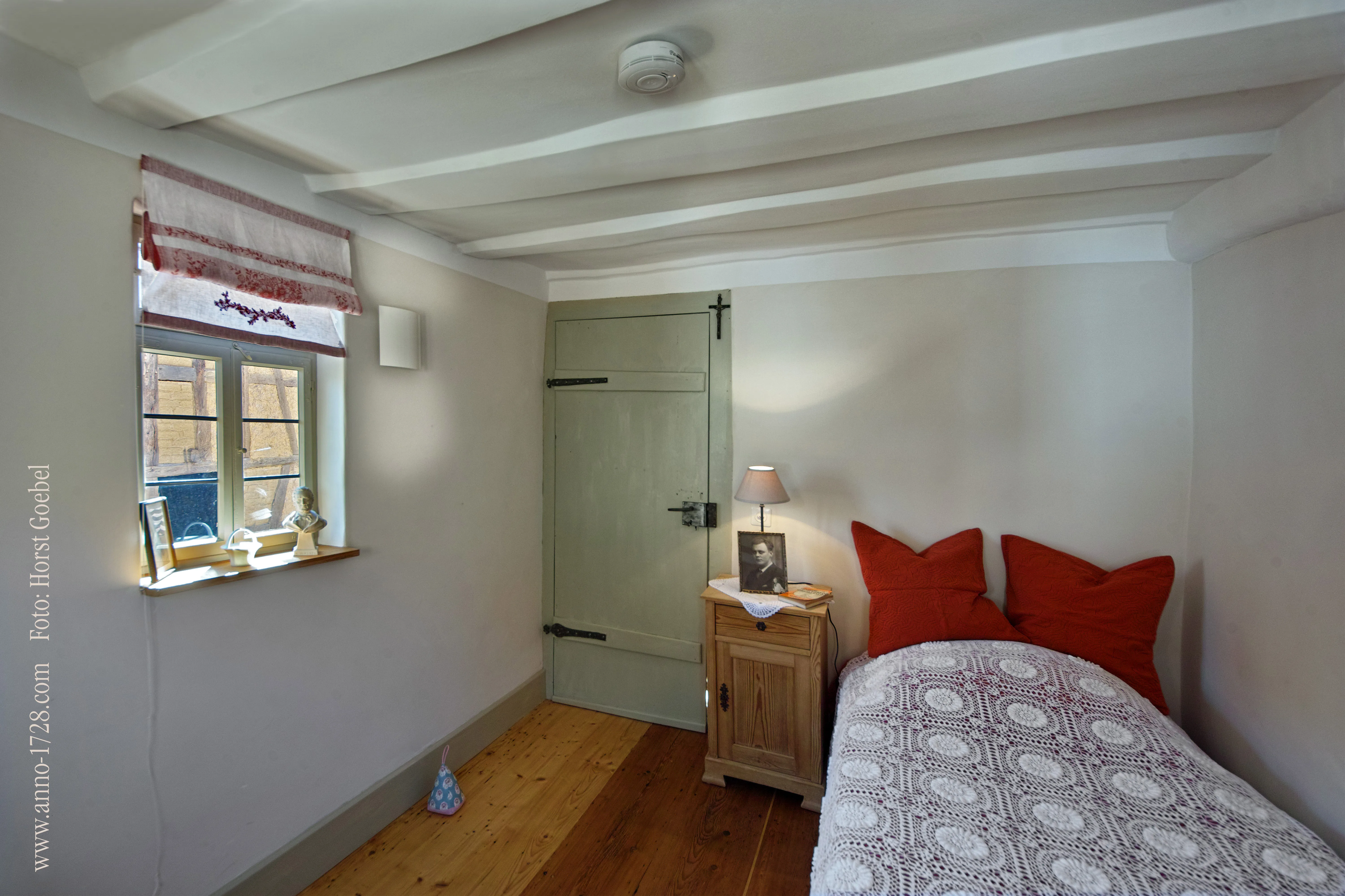 Kleines Schlafzimmer mit Einzelbett und historischer grüner Tür